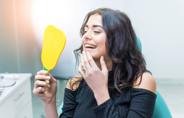 Young woman holding a mirror while looking at her new smile.